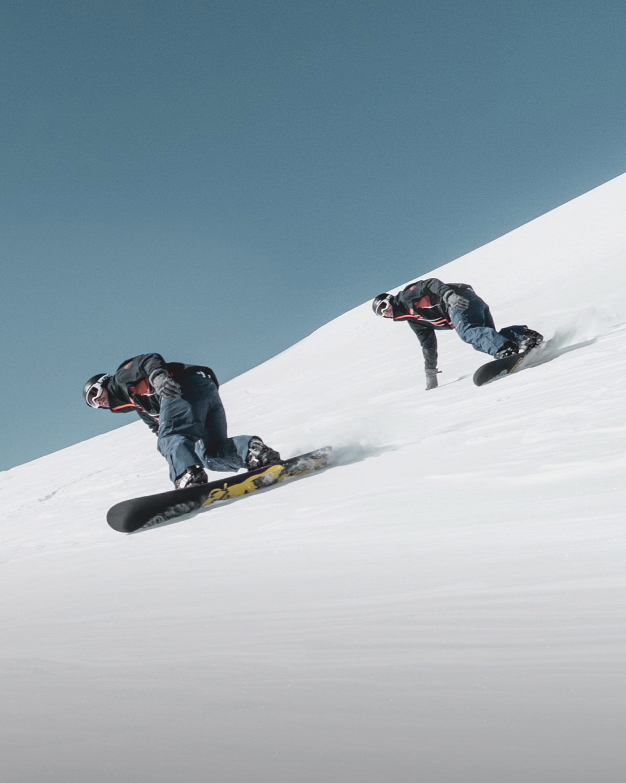 two snowbaorders turn down a groomed ski slope.