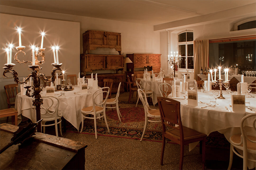 Interior shot of a dining room. There are rustic wood cabinets in the corner of the room and there are tall candelabras placed around the room in between the tables. The round tabled are donned in white linens and surrounded by white chira.