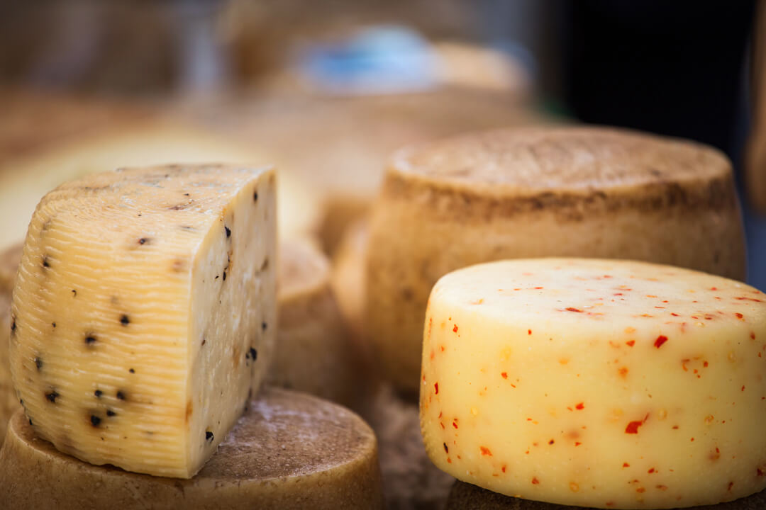 a detail shot of wheels of cheese. Each cheese wheel has different colors in it signifying the different flavors within the cheese.
