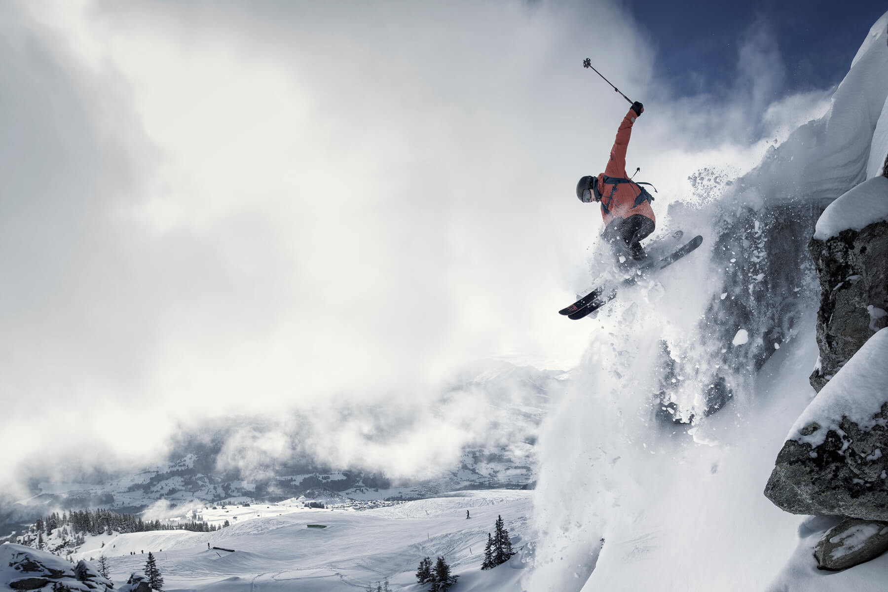 action shot of skier jumping off a snowy mountain and splashes snow and power, with blue sky, cloud and snowy mountain in the background