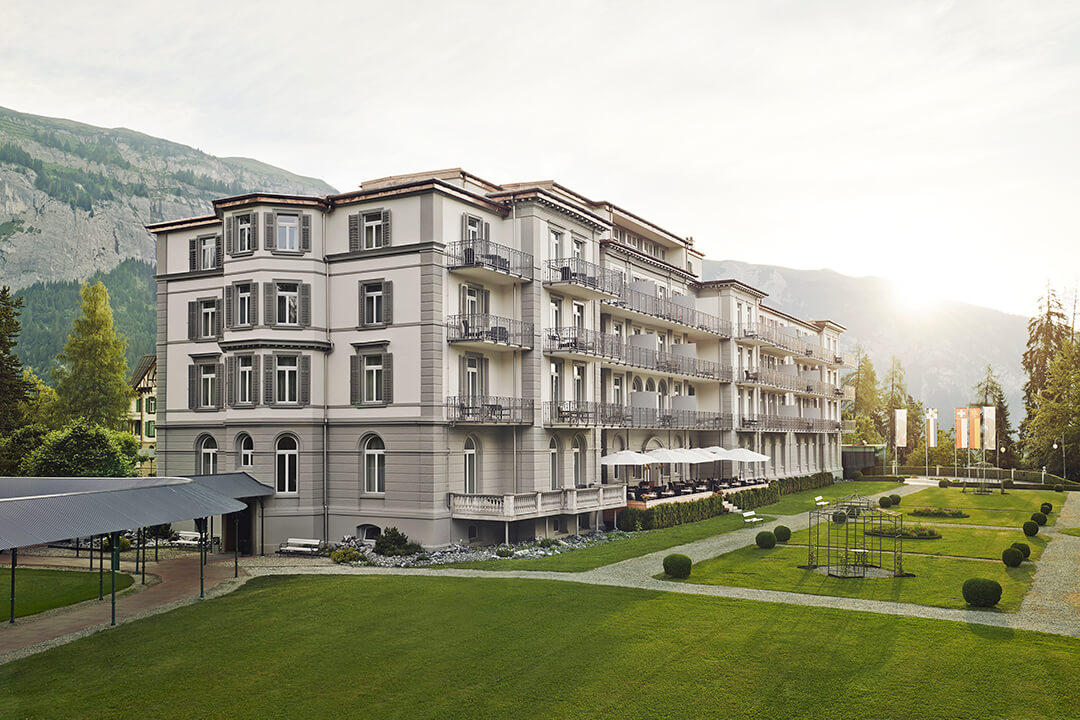 resort ground view of the Grand Hotel, Swiss Alps mountains, trees, sky and sun