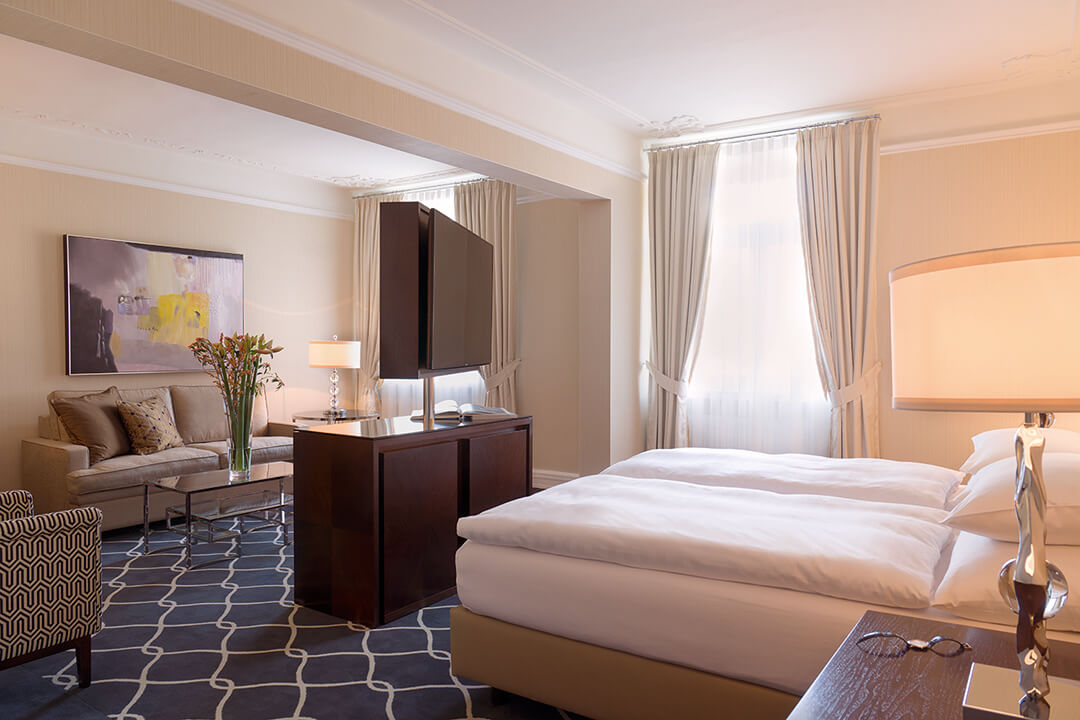 suite with white bed, sofa, chair, tv, and french door window opens to balcony