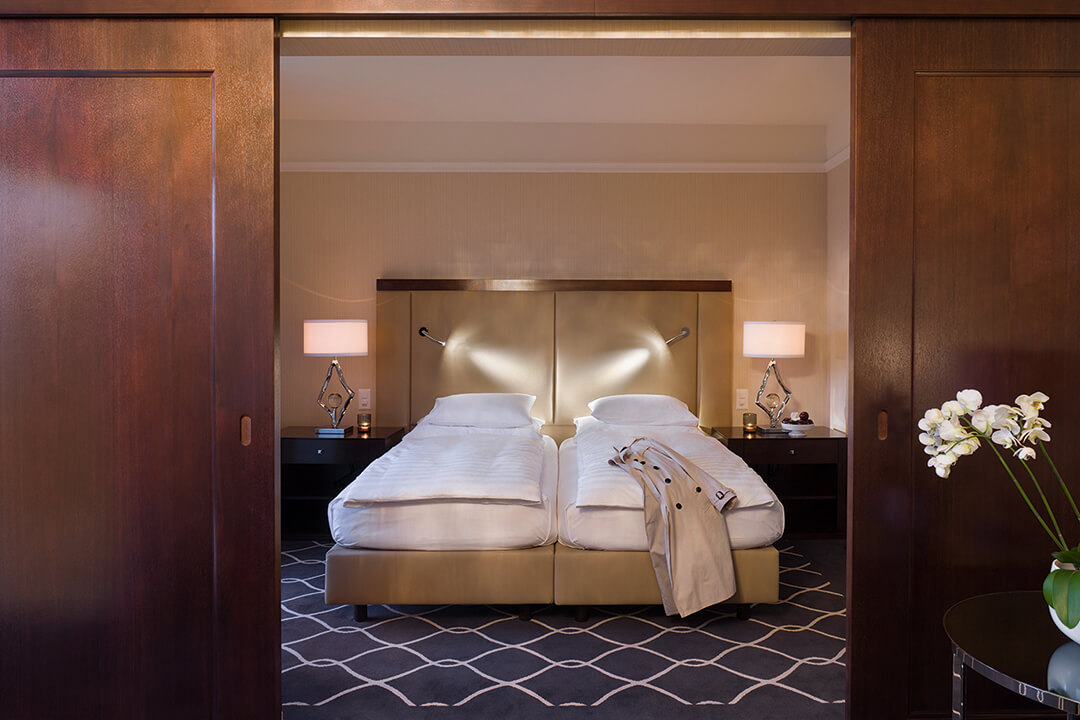 a two single bed room with white sheets and exposed wood beams overhead. There are two bedside tables with lamps on them. The room is accented with a light green color on the headboard.