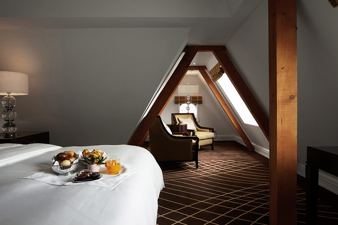 bedroom with charming wood beams, chairs, lamp and decor. breakfast, juice, fruits and flowers are on a tray on the bed