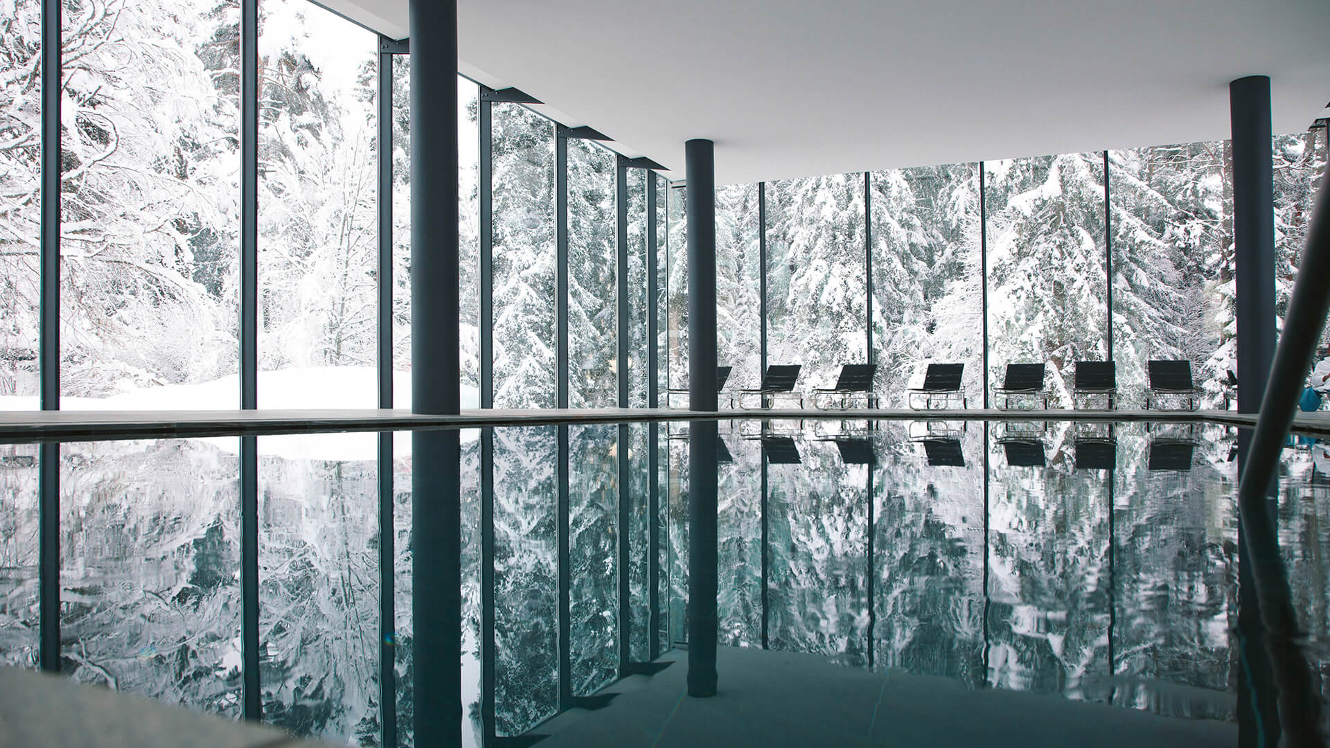 indoor pool with snow covered trees through the glass windows. the snow covered trees are reflected in the pool