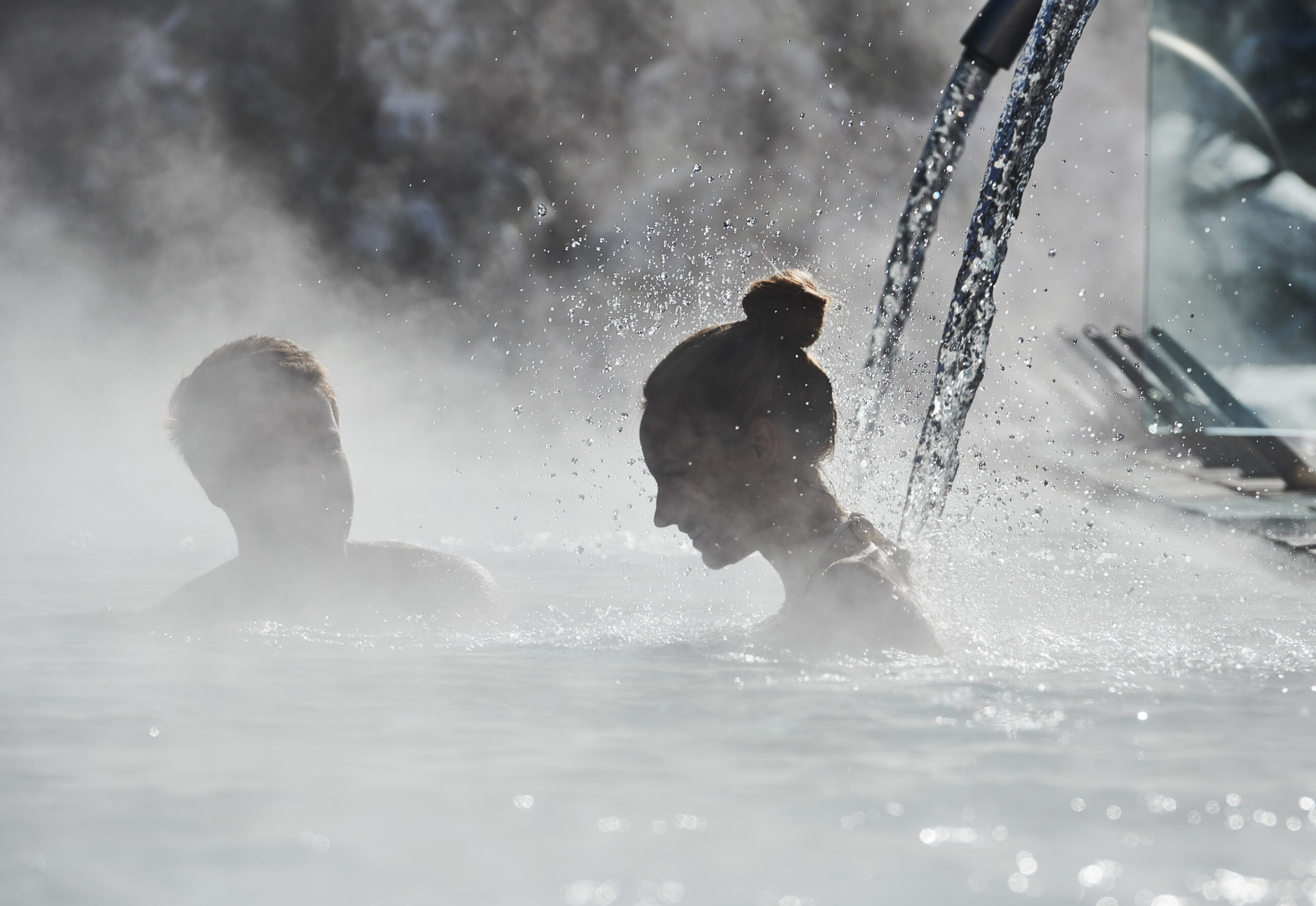 A couple relaxing under a stream of warm water in an outside heated pool